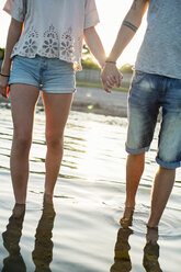 Tiefschnitt eines jungen Paares, das sich an den Händen hält und im Wasser am Strand spazieren geht - MASF06269