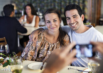 Happy young friends posing for photograph at restaurant table with people in the background - MASF06274