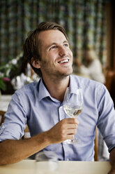Glücklicher junger Mann, der am Restauranttisch ein Weinglas hält und nach oben schaut - MASF06275