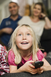 Kleines Mädchen mit Fernbedienung vor dem Fernseher und Eltern sitzen im Hintergrund - MASF06297