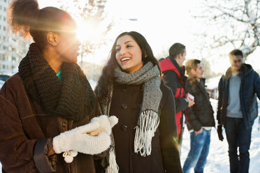 Glückliche junge Frauen in warmer Kleidung mit männlichen Freunden im Hintergrund - MASF06298