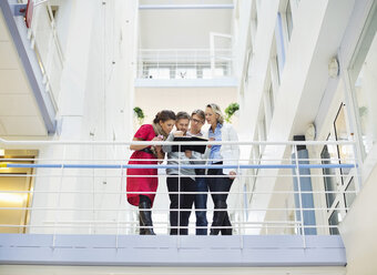 Low angle view of business people reading book together by railing - MASF06303