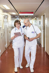 Männliche und weibliche Ärzte, die ein digitales Tablet benutzen, während sie durch einen Krankenhausflur gehen - MASF06321