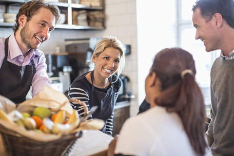 Männlicher und weiblicher Besitzer bedienen Kunden am Tresen eines Restaurants, lizenzfreies Stockfoto