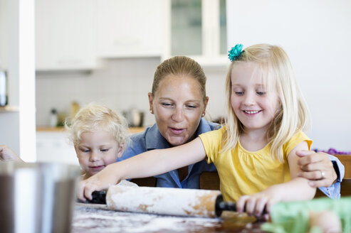 Glückliche Frau schaut auf ihre kleine Tochter, die auf dem Tisch in der Küche Teig ausrollt - MASF06335
