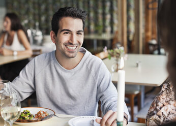 Glücklicher Mann, der seine Freundin am Restauranttisch mit Menschen im Hintergrund anschaut - MASF06337