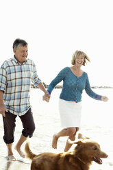 Happy couple running behind dog at beach - MASF06352