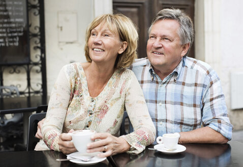 Glückliches Paar trinkt Kaffee und schaut dabei vom Tisch weg - MASF06356