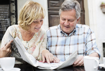 Glückliches Paar liest am Tisch Zeitung - MASF06357