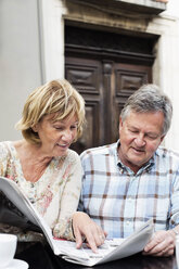 Happy couple reading newspaper at restaurant table - MASF06358