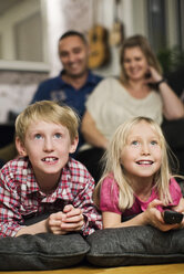 Glückliche kleine Geschwister vor dem Fernseher, die Eltern sitzen dahinter - MASF06376