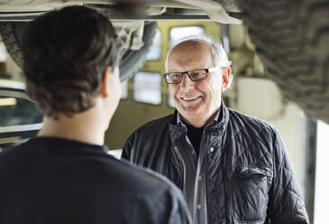 Glücklicher älterer Mann, der einen Mechaniker unter dem Auto in einer Autowerkstatt betrachtet - MASF06391