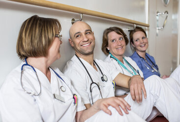 Happy male doctor and female colleagues leaning together on wall in hospital - MASF06392