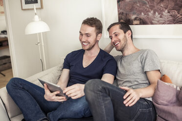 Glückliches homosexuelles Paar, das gemeinsam auf dem Sofa zu Hause ein digitales Tablet benutzt - MASF06393