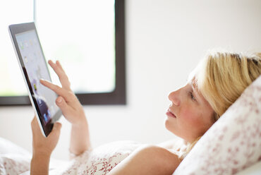 Lässige Frau im mittleren Erwachsenenalter, die auf ein digitales Tablet schaut, während sie auf dem Bett liegt - MASF06396