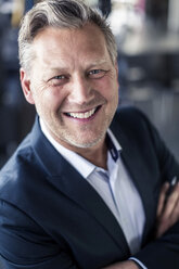 Close-up portrait of mature businessman standing arms crossed in office - MASF06414