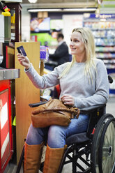 Disabled woman in wheelchair paying through credit card at supermarket - MASF06445