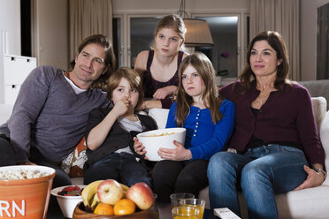 Fünfköpfige Familie mit einer Schüssel Chips vor dem Fernseher im Wohnzimmer - MASF06452