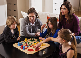 Familie spielt gemeinsam am Wohnzimmertisch Ludo - MASF06453