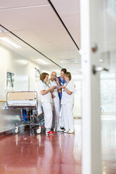 Vier Ärzte benutzen ein digitales Tablet, während sie auf einem Krankenhausflur neben einer Trage stehen - MASF06459