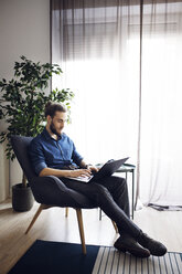 Man using laptop computer while sitting on chair at home - CAVF45016