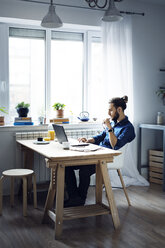 Man using laptop computer while sitting by window at home - CAVF45022