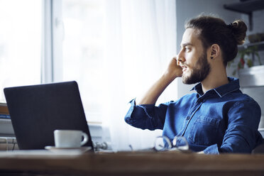 Man talking on mobile phone while sitting by window at home - CAVF45023