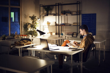 Man studying while sitting by table in library - CAVF45031