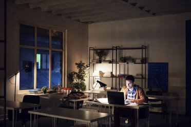 Confident student studying while sitting in library at night - CAVF45040