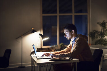 Side view of man studying through laptop computer in library at night - CAVF45041