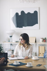 Smiling businesswoman writing while sitting at desk in office - CAVF45058