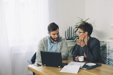 Colleagues discussing while sitting at table in office - CAVF45061