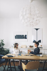 Businesswomen discussing while sitting at table in office - CAVF45063