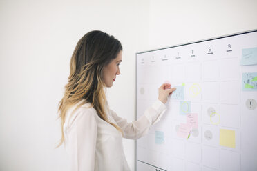 Side view of businesswoman sticking adhesive notes on whiteboard in office - CAVF45077