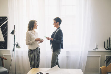 Geschäftsfrauen im Gespräch, während sie vor einem Vorhang im Büro stehen - CAVF45091