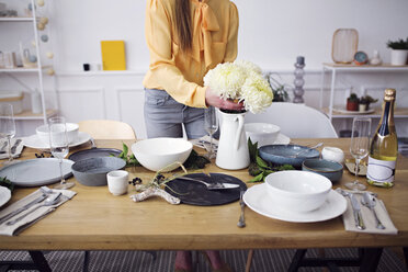 Low section of woman arranging flowers at dinning table in home - CAVF45098