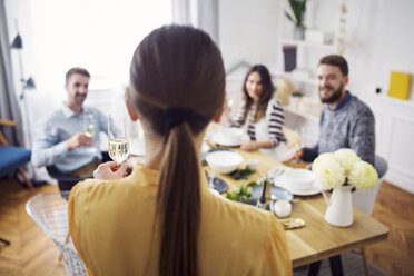 Rückansicht einer Frau, die eine Sektflöte hält, während Freunde am Tisch sitzen - CAVF45103