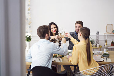 Glückliche Freunde stoßen mit Sektflöten an, während sie am Esstisch sitzen und zu Mittag essen - CAVF45109