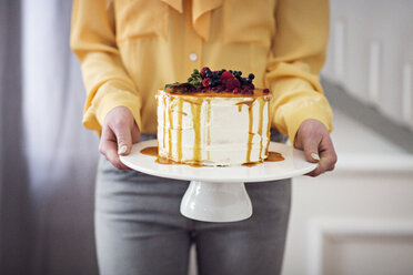 Mittelteil einer Frau, die zu Hause einen Kuchen auf einem Ständer hält - CAVF45121