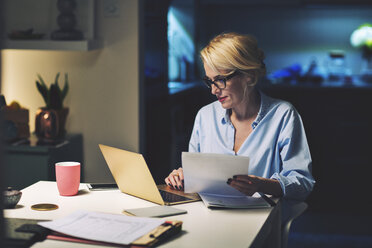 Geschäftsfrau mit Dokument, die bei der Arbeit zu Hause einen Laptop benutzt - CAVF45153