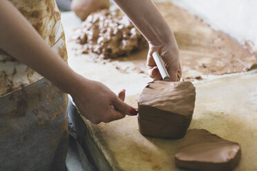 Midsection of female potter making clay on table in workshop - CAVF45157