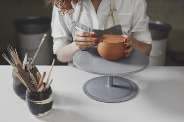 Midsection of female potter molding shape to clay with work tool at table - CAVF45170