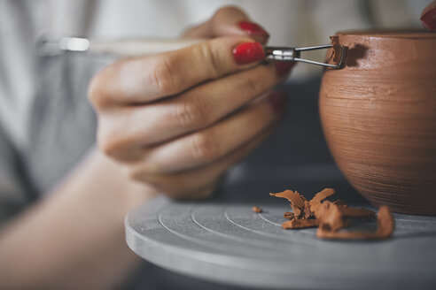 Close-up of female potter molding shape to clay with work tool in workshop - CAVF45171