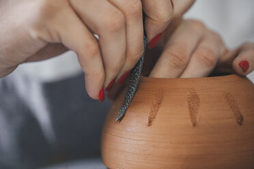 Abgeschnittene Hände einer Töpferin, die einen Topf in einer Werkstatt dekoriert - CAVF45173