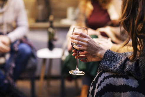 Abgeschnittene Hände einer Frau, die ein Weinglas hält, während sie in der Abenddämmerung im Hinterhof sitzt - CAVF45193
