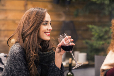 Happy woman enjoying wine while sitting in backyard at night - CAVF45204