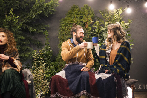 Smiling friends toasting drinks while sitting in backyard at night - CAVF45205