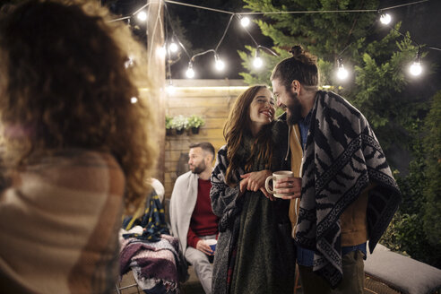 Romantic couple enjoying party with friends in backyard at night - CAVF45216