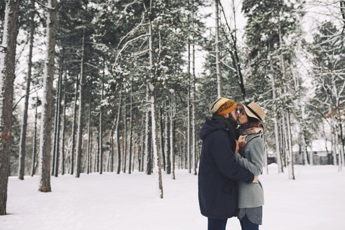 Romantisches Paar, das sich küsst, während es auf einem schneebedeckten Feld im Wald steht - CAVF45224