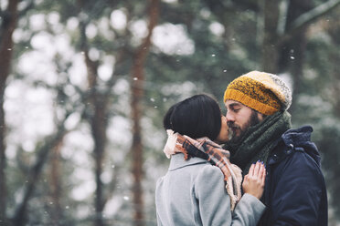 Romantic couple kissing while standing in forest during winter - CAVF45225